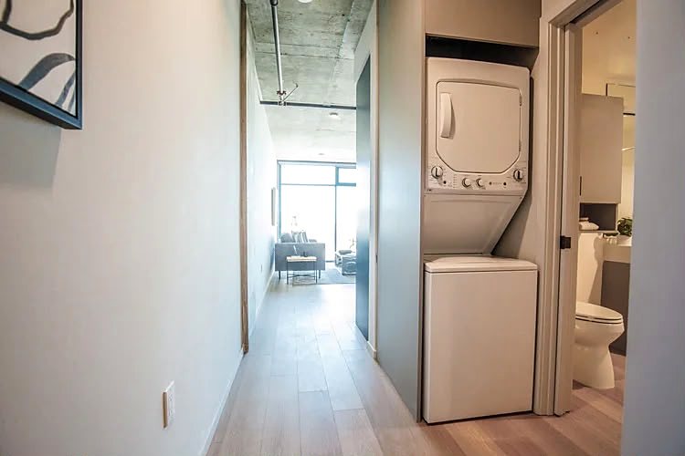 Hallway with a stacked washer and dryer in a cabinet recess and the guest bathroom door alongside.