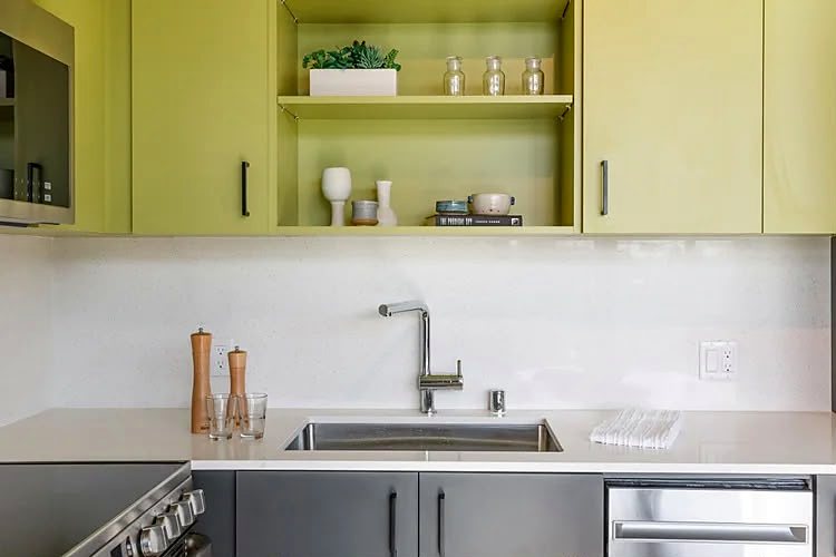 Close view of a kitchen run: open shelving above the counter, a slab backsplash and a tall gooseneck tap.