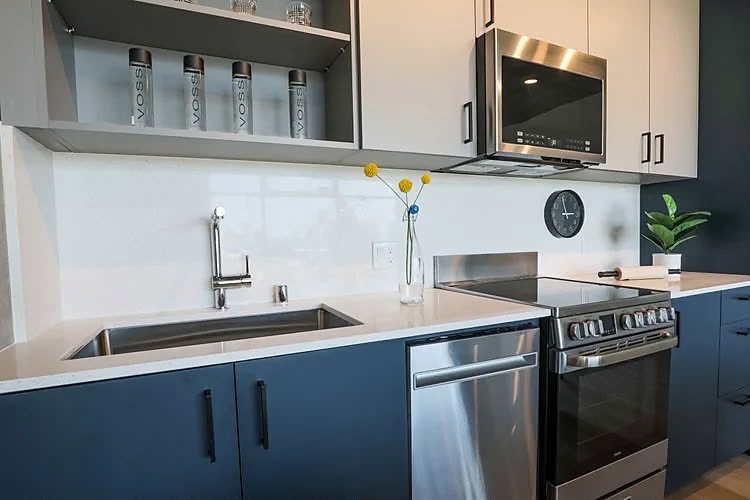 Kitchen with navy slab-front cabinets, quartz counters, stainless appliances and an undermount sink.