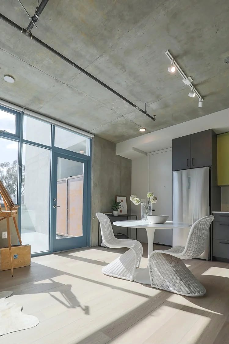 Dining area of a finished studio unit, with a terrace door and afternoon light across a pale timber floor.